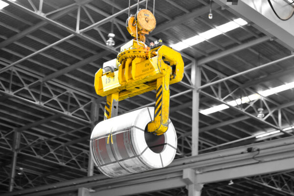 Overhead crane lift up steel coil with tong in warehouse. Steel coils handling equipment. Steel warehouse and logistics operations.